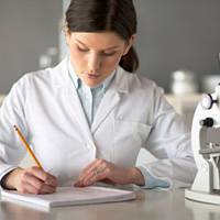 Female\ scientist\ sitting\ by\ microscope\,\ writing\ in\ notebook\,\ close\-up
